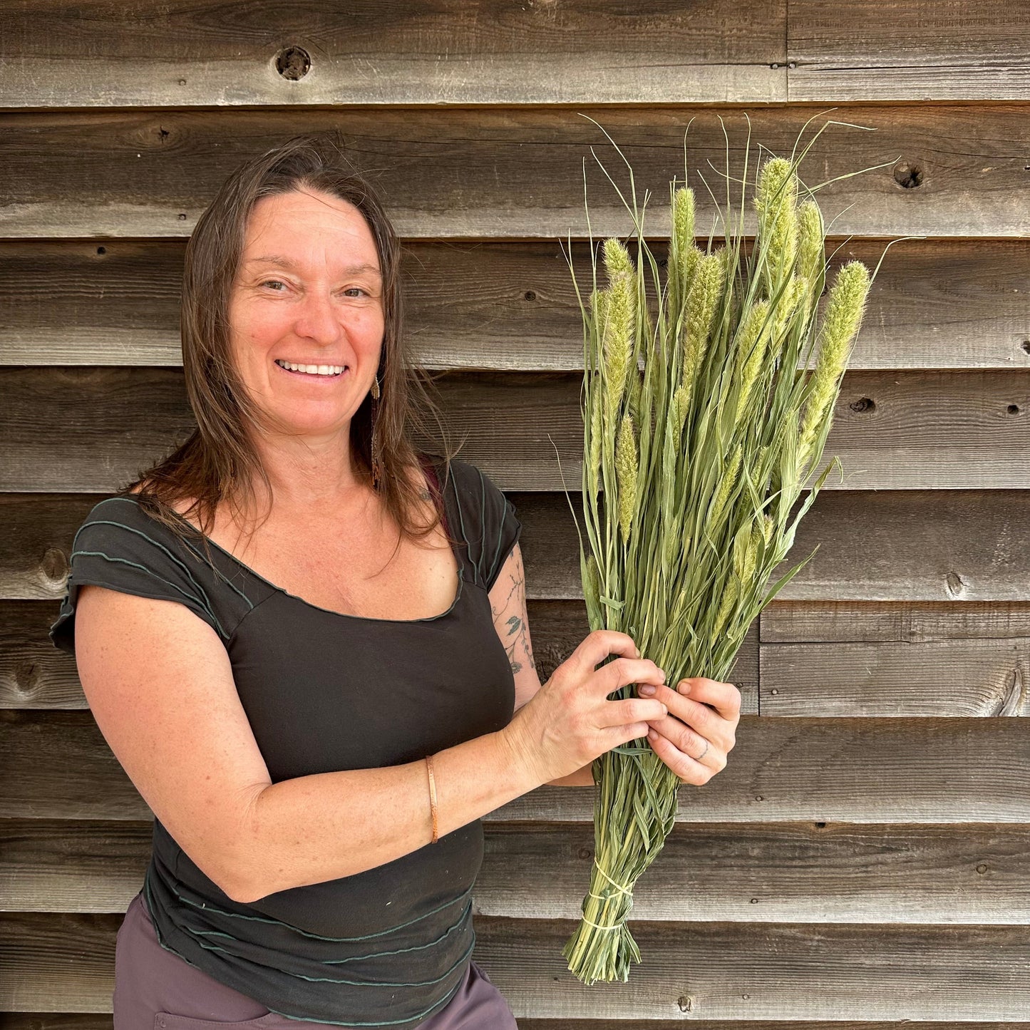Woman holding dried foxtail grass against a wooden bakcground