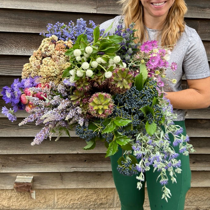 Woman holding a large bouquet of flowers against a wooden wall.
