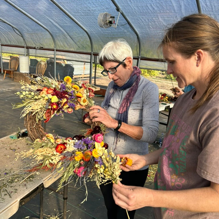 Two people working on a floral wreath in a greenhouse.