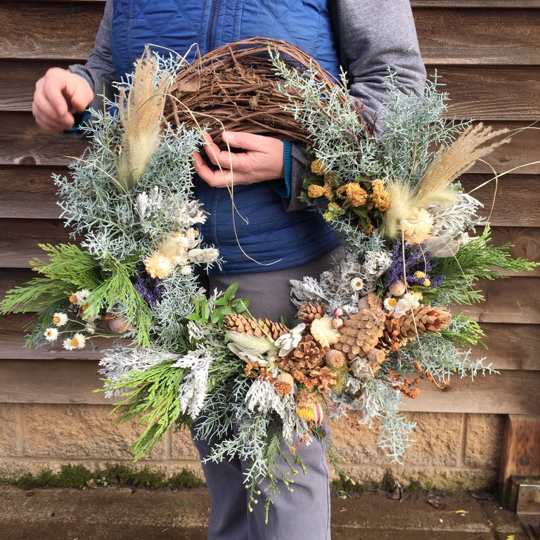 Person holding a large decorative wreath against a wooden wall.