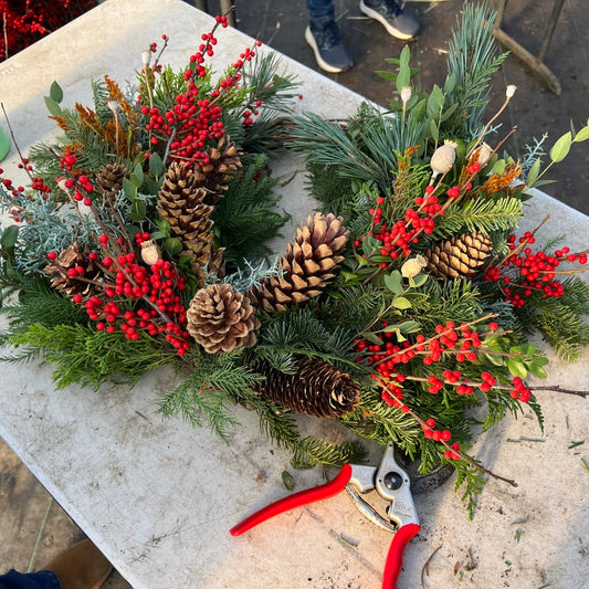 Christmas wreath with pine cones and red berries on a table with pruning shears nearby.