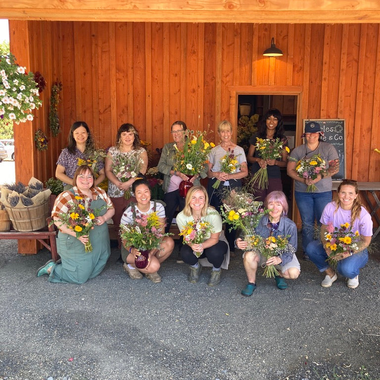 Group of people holding flower bouquets in front of a wooden building