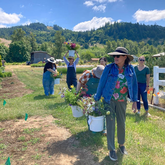 People on a farm holding buckets of flowers on a sunny day with mountains in the background