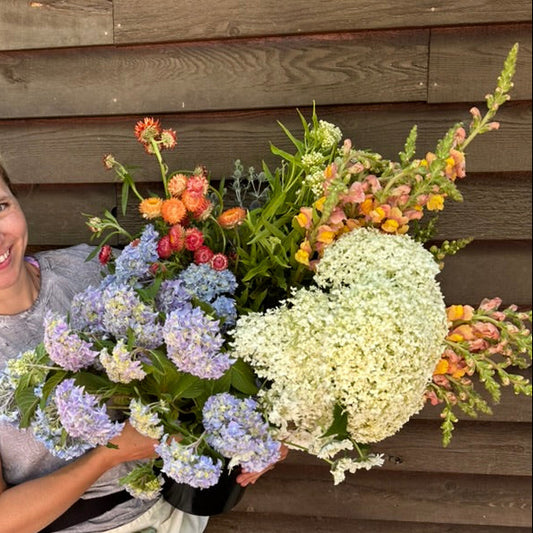 Woman holding a large bouquet of wildflowers against a wooden wall.