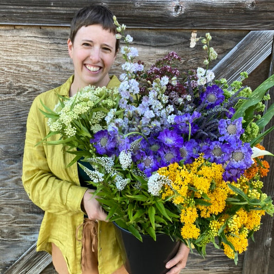 Person holding a large bouquet of wild-flowers against a wooden background
