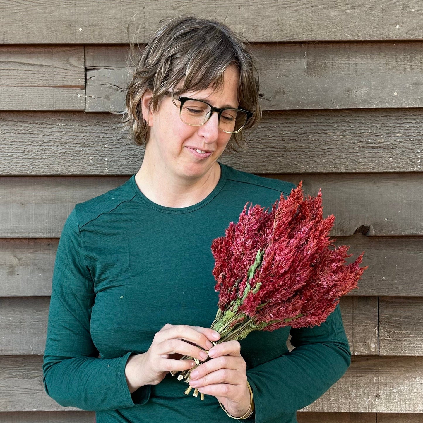 Person holding a bundle of red flowers against a wooden wall